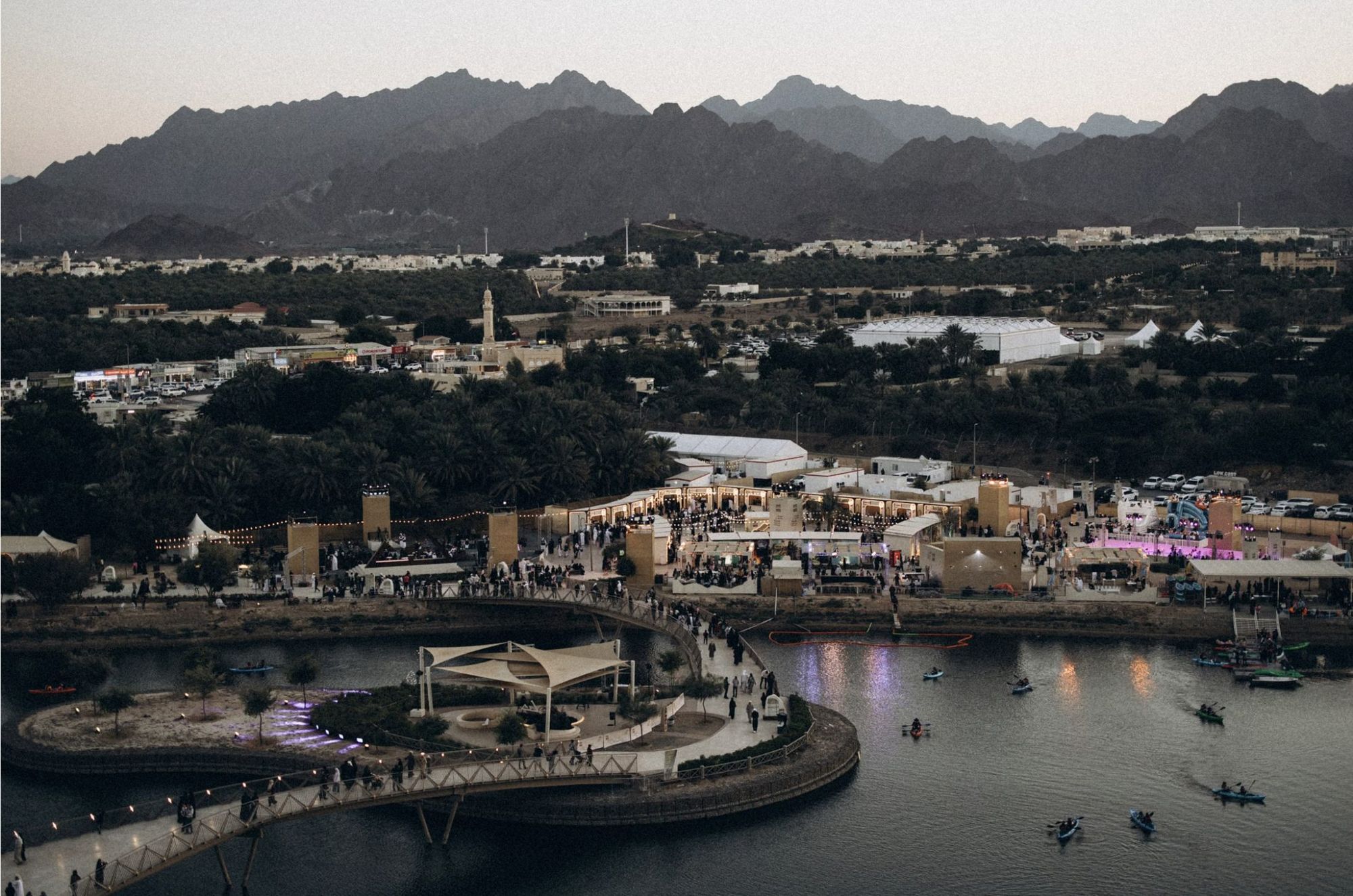 Kayaks on the Hatta reservoir at dusk, with a lit market and the mountains behind